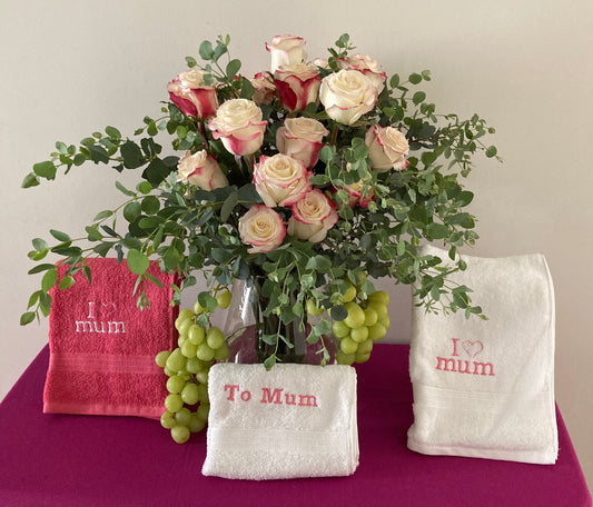 Bouquet of flowers with three towels embroidered with 'I love mum' on a purple surface.